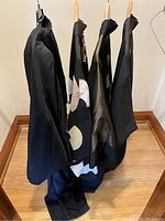 Four kimono style jackets hanging on wooden and wire hangers on a wood floor next to a wall.