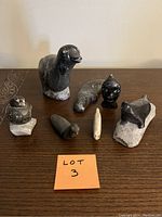 Top view of all seven sculptures arranged on wooden table with handwritten 'Lot 3' note in front. Shows size and shapes.