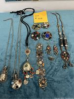 Large lot of vintage Bohemian estate jewellery laid out on blue surface including multiple necklaces, bracelet, pins, earrings, and ring.