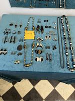 Photo shows a spread of multiple pairs of earrings, necklaces, a scarab pendant, and brooches all primarily black in color with some grey and silver beads visible.