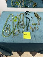 Overview of the lot laid out on a blue surface showing multiple green jewelry items including necklaces, bracelets, earrings, and the fish hook pendant necklace.