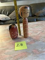Front view showing both dolls side-by-side with measuring tape indicating their height and a numbered sticky note '28' in front