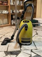 Front view of yellow Miele Complete C3 canister vacuum with attached hose, wand and floor nozzle on tiled floor