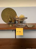 Front view of brass peacock with outspread feathers and pressed glass bowl holding rocks on shelf