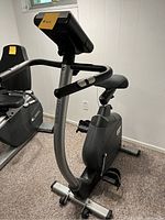 Angled side view of stationary exercise bike showing the seat, pedals, and part of the frame and digital console