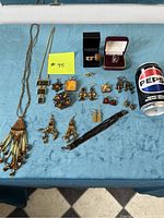 Overview of the vintage jewellery collection arranged on blue fabric with a Pepsi can for size reference. Includes various rings, earrings, pendants, bracelet, and statement necklace with dangling beads and metal rods.