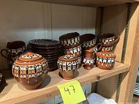 Shelf with all matching pottery pieces arranged, showing mugs, plates, small vase, sugar bowl, and creamer with ornate hand-painted design.