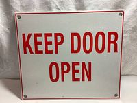Photo of front side of the metal door sign reading 'KEEP DOOR OPEN' in bold red letters with white background and red border.