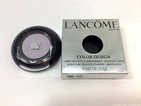 Front view of the closed lavender eye shadow compact and the silver product box with brand and product name.