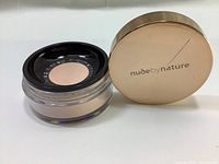 Top and side view of the Nude By Nature translucent loose finishing powder container with lid off showing the powder and the sifter inside.