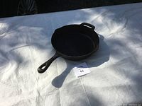 Cast iron frying pan on white surface, showing pan and handle in shadow.