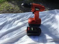 Black & Decker cordless drill with one battery placed beside it on white surface outdoors