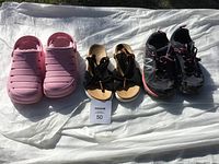 Lot of three pairs of shoes: pink Crocs, black and brown Grizzleez sandals, black New Balance running shoes; all appear used.