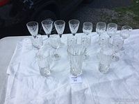 Overview of all 16 crystal glassware pieces arranged on a white cloth on a table outdoors.