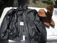 Black leather Ford coat XXL and brown Boulet cowboy boots size 11 EM displayed on a white surface in sunlight