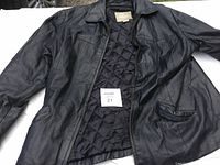 Image showing full front view of the black ladies leather coat laid flat, partially open to show lining and zipper