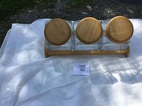 Set of three glass jars with wooden lids mounted on a wooden base, viewed from above.