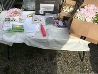 Overview of various party supply items spread on a table including bamboo cheese board box, artificial flowers, cloth napkins, and small utensils.