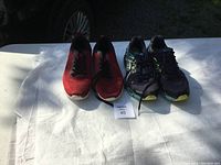 Two pairs of running shoes, one red and one black with green and blue accents, shown side by side on a white surface.