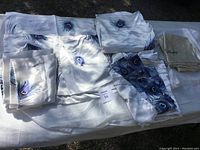 Satin sheets and pillowcases laid out showing peacock feather design on white satin.