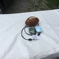 Football shaped Scentsy warmer with attached black power cord and on/off switch, placed on white cloth background. Two scented wax bars in green and light blue colors shown beside warmer.