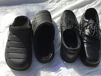 Photo showing two pairs of men's size 12 shoes: black slip-on clogs with fur lining and black lace-up dress shoes side by side, taken under natural light.