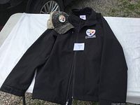 The full black Steelers coat laid out on a white cloth with the camouflage cap placed above the left shoulder area.