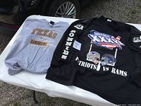 Two XXL sports shirts laid out flat: Black Super Bowl XXXVI long-sleeve and grey Texas Longhorns short-sleeve shirt.