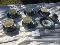 Full view of six blue and white porcelain tea cups arranged on matching saucers laid out on a white cloth, showing uniform design and consistent pattern across cups and saucers.
