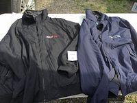Two jackets laid flat on a surface outdoors. One jacket black with Teo Pro logo, other navy blue also with logo.