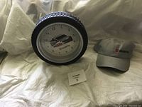 Clock shaped like a tire with white clock face showing a car image and Wurth logo alongside a grey Wurth ball cap. Both displayed on white fabric background.
