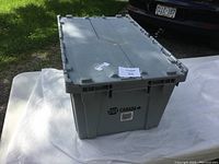 Closed top view of a large gray GPS Canada plastic tote with hinged lid on white cloth outdoors.