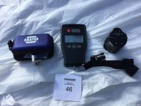 Photo of Northern Traveller digital luggage scale with display showing 0.00 and strap, next to the international plug adapter and NAPA branded case with plug adapter inside.
