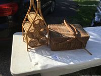 Photo showing both the wicker picnic basket and wicker wine rack placed on white table outdoors.