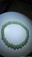 Natural green aventurine beaded bracelet on a white circular surface, round polished beads in light green translucent color.