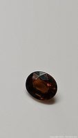 Oval cut orange tourmaline gemstone with a medium deep orange-brown hue shown at an angle on a white background.