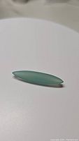 Natural marquis cut arctic blue-green chalcedony gemstone lying on a white surface in natural diffuse light, showing coloration and shape.