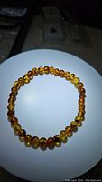 Photo of a Baltic amber stretchy bracelet laid flat in a circle on a white round surface against a dark background. Shows amber beads with mixed translucent yellow and brown colors and natural inclusions.