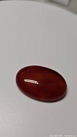 Oval polished Carnelian gemstone with deep red-orange color on white background.