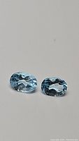 Pair of oval sky blue topaz gemstones on a neutral background.