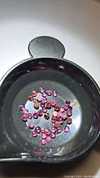 Photo showing multiple small round cabochon rhodolite garnet stones in a black container, colors range from pink to reddish-purple with some visible inclusions.