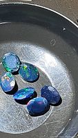 Six polished and faceted Ethiopian black opals displayed on a round dark dish surface showing play of color under light.