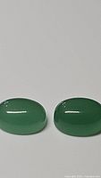Pair of large oval cabochon green onyx gemstones on white background with close lighting.