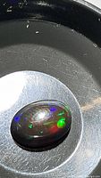Close-up image of oval cabochon Ethiopian black opal displaying bright flashes of green, blue, purple, and other colors on a dark black base.