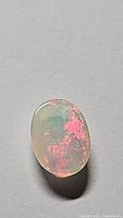 Oval cabochon cut Ethiopian opal gemstone displaying translucent body with multicolored rainbow flash mainly in red and green hues.