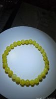 Photo of the Lemon Jade bracelet placed on a white circular surface showing uniform round bright yellow beads.