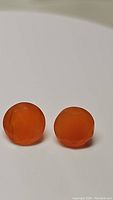 Pair of round faceted Mandarin orange carnelian gemstones on white background.