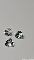 Three natural aquamarine gemstones arranged on a neutral background showing the trillion cut and light blue color.
