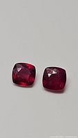 Close-up image of a pair of natural blood red cushion cut rubies placed on a white background.