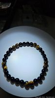 Photo showing full view of the bracelet with alternating black onyx and tiger's eye beads on white surface under spotlight.